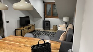 A modern living room with a wooden dining table, a sofa, a TV, and a fireplace.