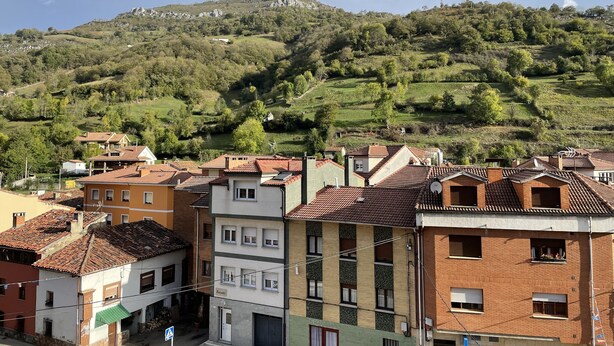 A residential area with terraced houses, a hillside with greenery, and a clear sky.