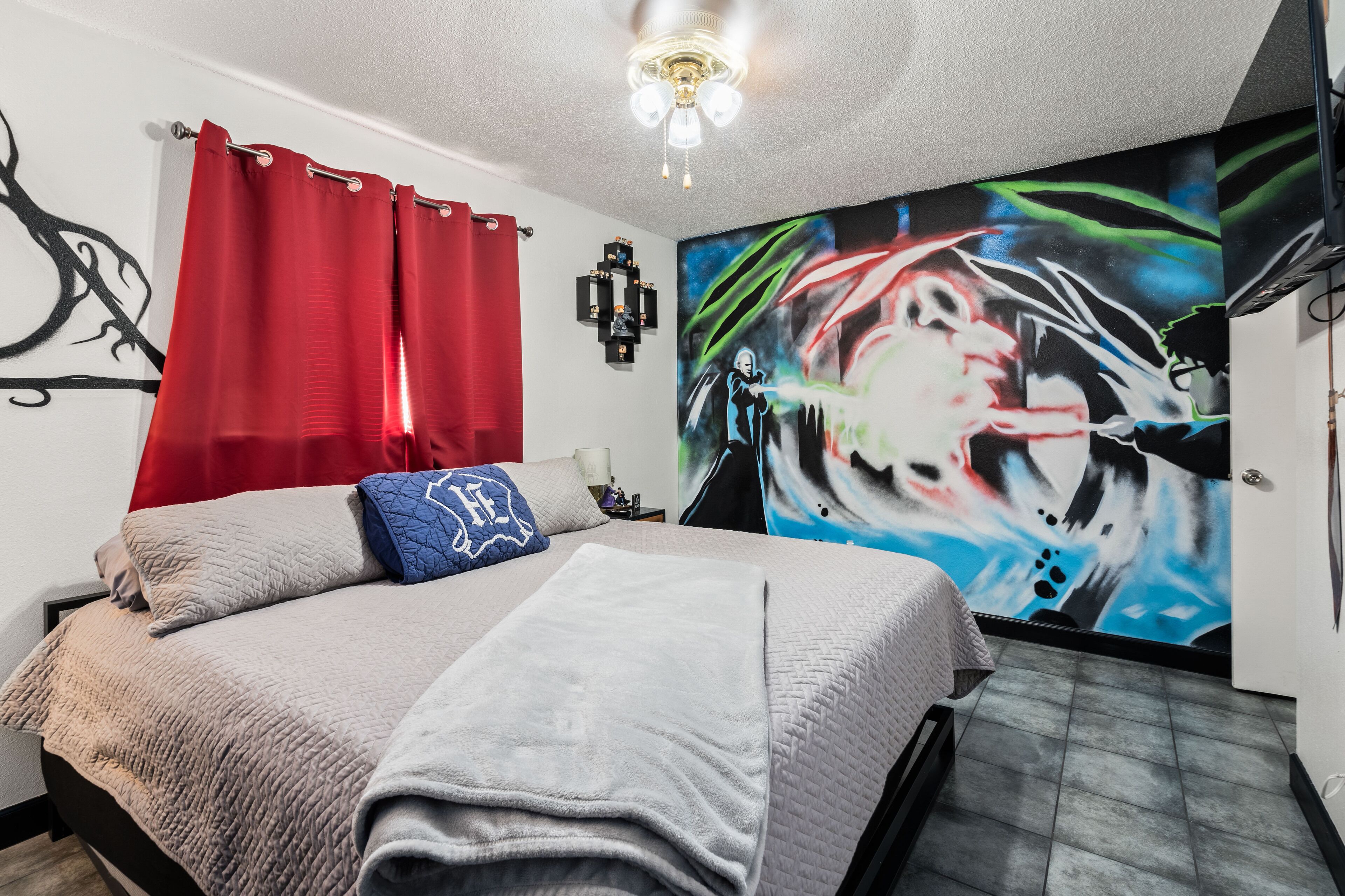 Un dormitorio con cama, cortinas rojas, un mural en la pared y un ventilador de techo.