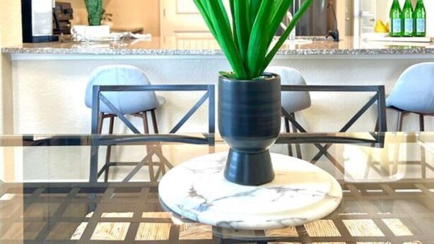 Eine moderne Küche mit dunklen Schränken, einer Marmorarbeitsplatte und einem Blumentopf auf einem Glastisch.
