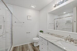 Une salle de bain moderne avec une douche à parois de verre, des toilettes blanches, un lavabo en marbre et un grand miroir.