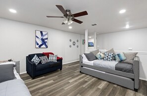 Un salon moderne avec deux canapés, un ventilateur de plafond et un grand tableau abstrait accroché au mur.