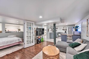 Een moderne woonkamer met een bank, een bed, een televisie en een keuken in de achtergrond.