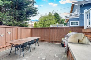 Een achtertuin met een houten tafel en stoelen, een barbecue en een houten omheining.