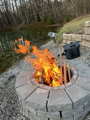 A fire pit with logs, surrounded by a stone wall and a bag nearby. - Warm and inviting, close to the best New England hiking and outdoor fun! (Bartlett)