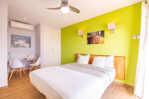 Een hotelkamer met een bed, een bureau met stoelen, een plafondventilator en kunstwerken aan de wanden.