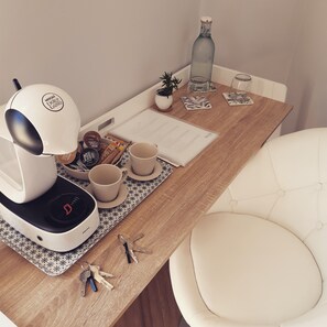 Een netjes opgeruimd werkplek met een koffieapparaat, kopjes, een fles, sleutels en een kleine plant op een houten tafel.