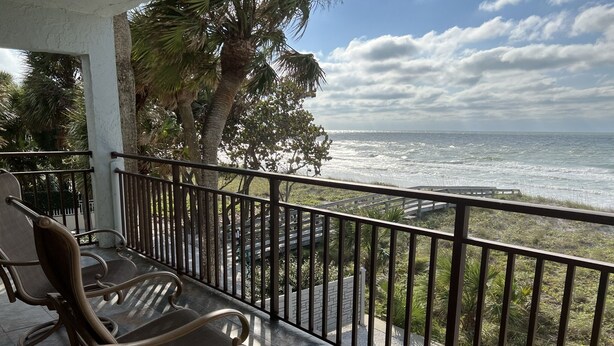 Een balkon met twee rieten stoelen, uitzicht op de oceaan en palmbomen.