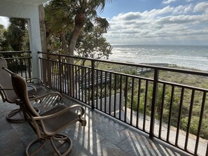 A balcony with two wicker chairs, a view of the ocean, and palm trees.