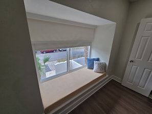 A room with a built-in bench under a window, a door, and a view of the street outside.