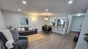 A modern living room with a grey sofa, a dining area with a table and chairs, and a kitchen in the background. - Luxurious & Spacious Townhouse in Prime Location (Miami)