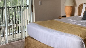 Hotellihuone, jossa on suuri sänky, seinällä taulu, lamppu ja parveke, jolta on näkymä puustoon.