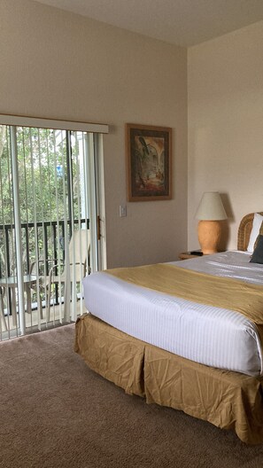 A hotel room with a large bed, a painting on the wall, a lamp, and a balcony with a view of trees.