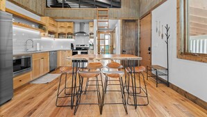 A modern kitchen with wooden cabinets, a central island with stools, and a lofted sleeping area.