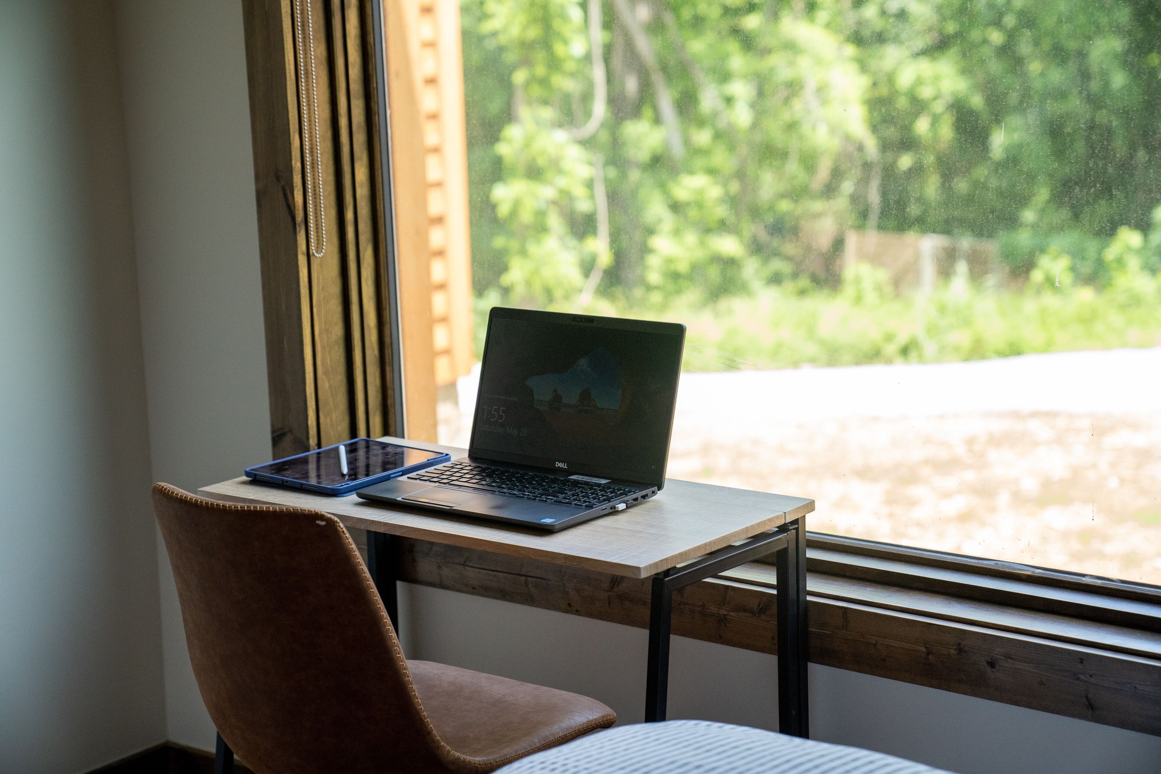 Una computadora portátil sobre un escritorio de madera cerca de una ventana con vista a follaje.