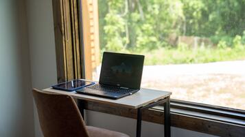 Una computadora portátil sobre un escritorio de madera cerca de una ventana con vista a follaje.