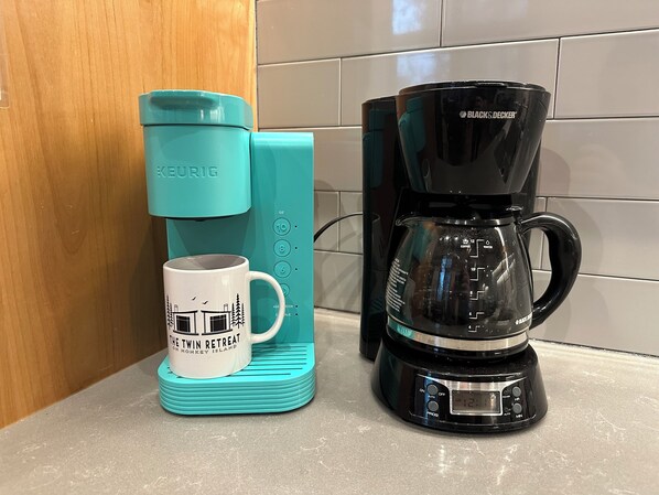Una cocina con una cafetera Keurig color turquesa, una cafetera Black & Decker negra y una taza sobre un posavasos turquesa.