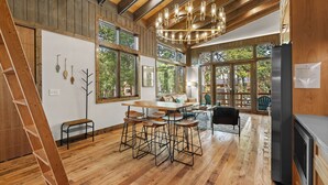 A spacious kitchen with wooden floors, a dining area with bar stools, large windows, and a modern chandelier.