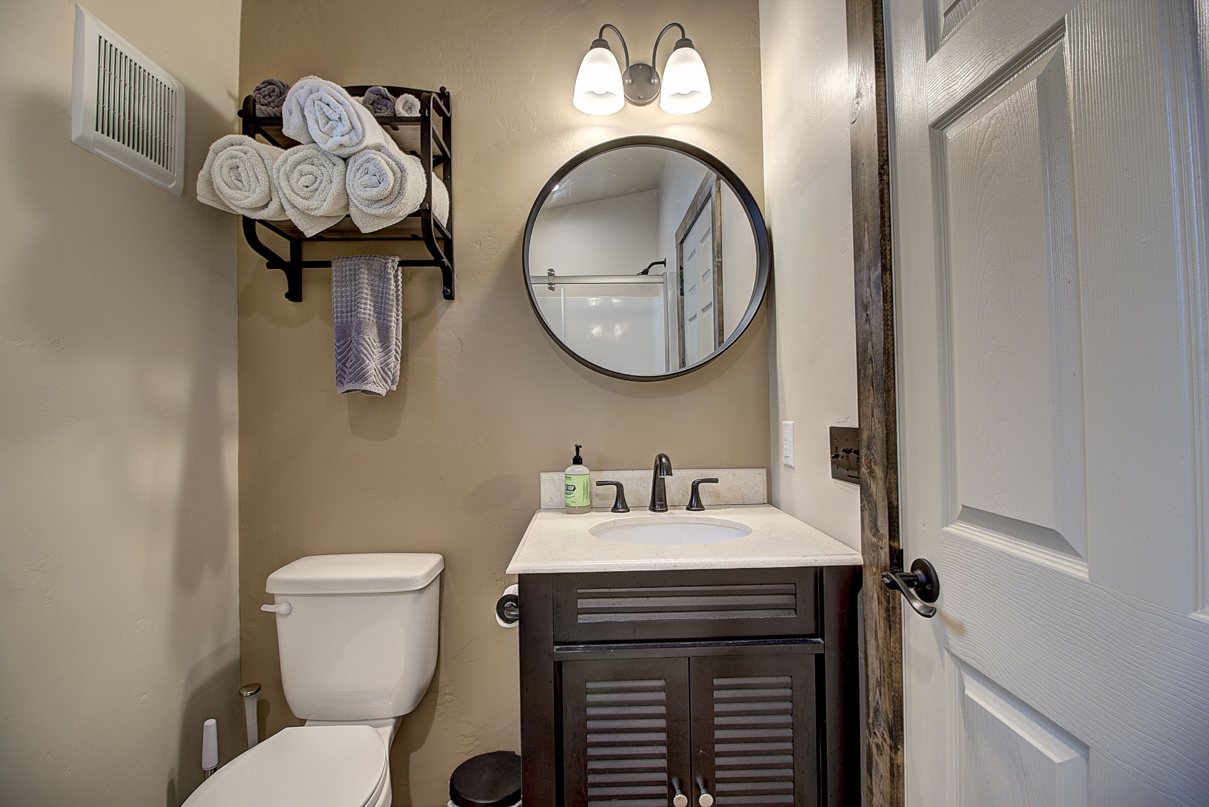 A bathroom with a toilet, sink, mirror, towel rack, and a door.