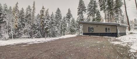 Une petite cabane avec une allée de gravier et des arbres couverts de neige en arrière-plan.