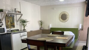 Kompakti hotellihuone, jossa on pieni keittiö, ruokailutila ja sänky, jonka pääty on vihreä.