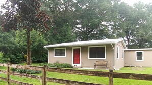 A single-story house with a red door, a small porch, and a wooden fence in front.