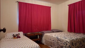 A bedroom with two single beds, a nightstand, and a Mickey Mouse plush toy on the left bed.