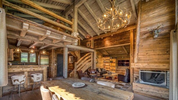A rustic log cabin interior with a dining area, bar, and fireplace.
