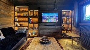A cozy living room with a wooden interior, a flat-screen TV mounted on the wall, a comfortable sofa, and a coffee table with a bowl of pinecones.
