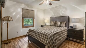 Une chambre à coucher avec un lit, une table de chevet, une lampe, un ventilateur de plafond et une fenêtre.