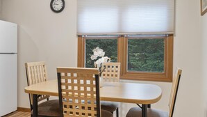Un coin repas avec une table et des chaises, une horloge au mur et une fenêtre donnant sur un paysage verdoyant.