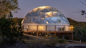 Una estructura de domo geodésico con una terraza de madera y luces colgantes.