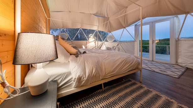 Una habitación con tienda de campaña, una cama, una lámpara y vistas al exterior.