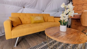 A yellow sofa with a white cushion, a wooden coffee table with a white vase of white flowers, and a patterned rug.