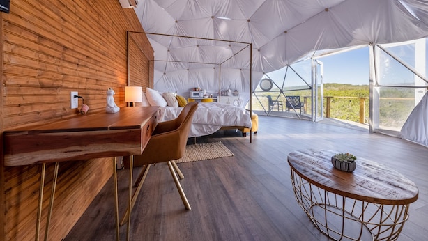 A modern tented accommodation with a wooden interior, a dining area, and a view of the landscape.