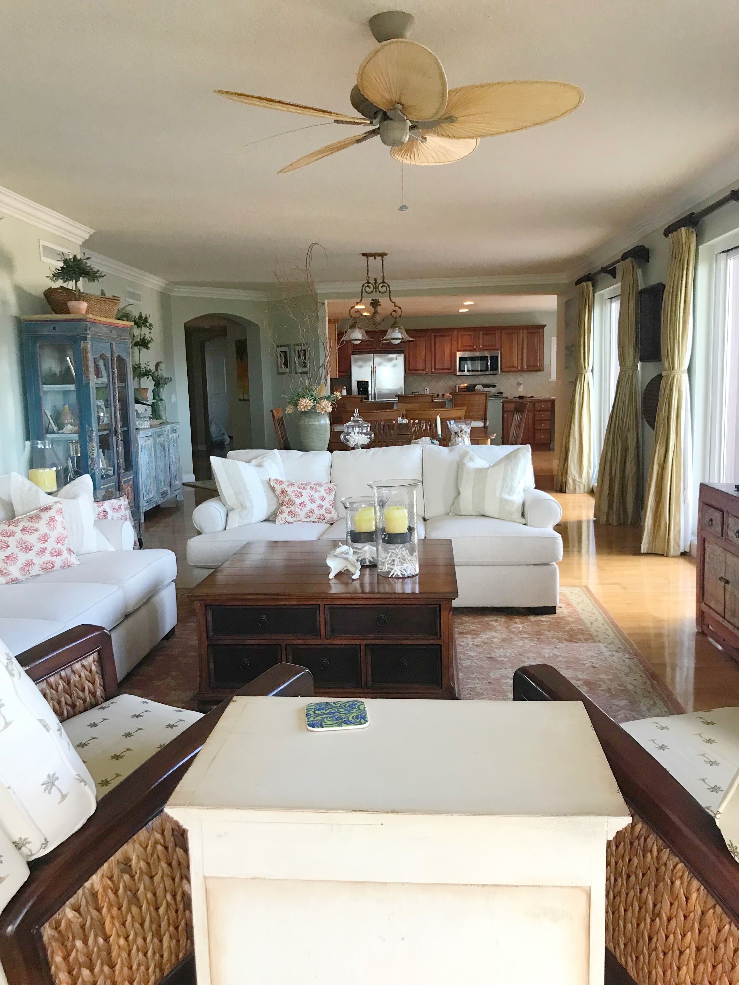A spacious living room with a ceiling fan, a dining area with a table and chairs, and a kitchen in the background.