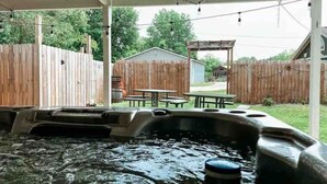 A hot tub area with a wooden fence, a covered patio, and a table and chairs in the background.