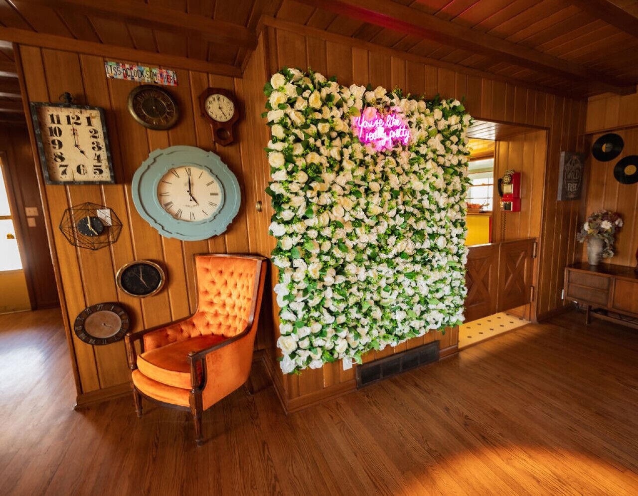 Une pièce aux murs en bois, ornée d’un motif floral, avec une horloge ancienne et un fauteuil orange à motifs.