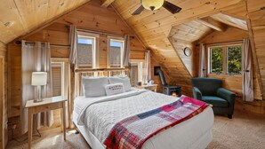 A cozy attic bedroom with a bed, a chair, a heater, and a window with curtains. - The Bucking Moose (West Yellowstone)