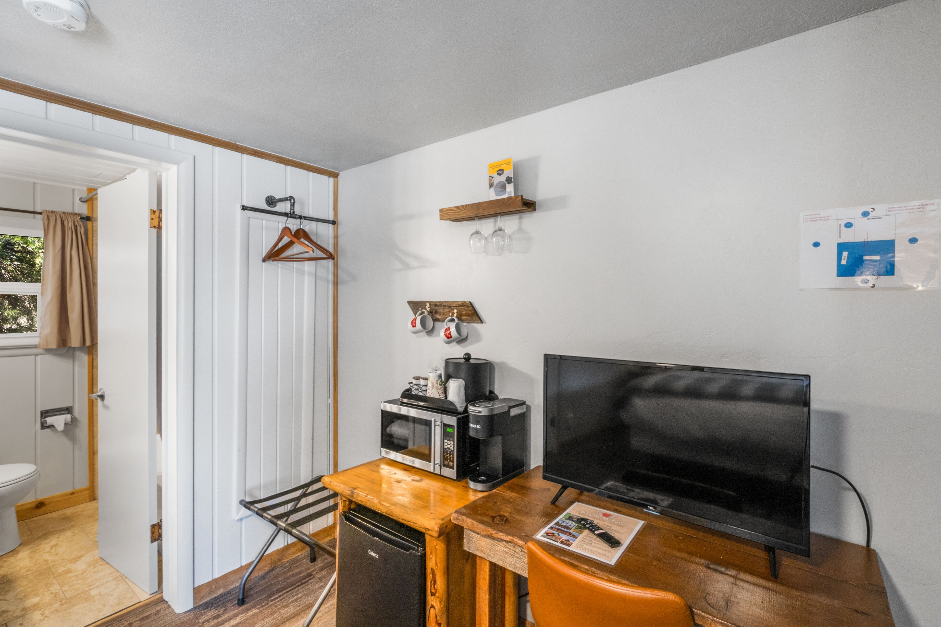 A compact room with a wooden desk, a television, a microwave, and a coffee maker.