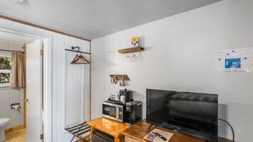 A compact room with a wooden desk, a television, a microwave, and a coffee maker.