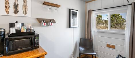 Eine Küche mit Mikrowelle, Kaffeemaschine und einem Holzkasten. Ein Stuhl und eine Bank befinden sich in der Nähe eines Fensters mit Blick auf Bäume.