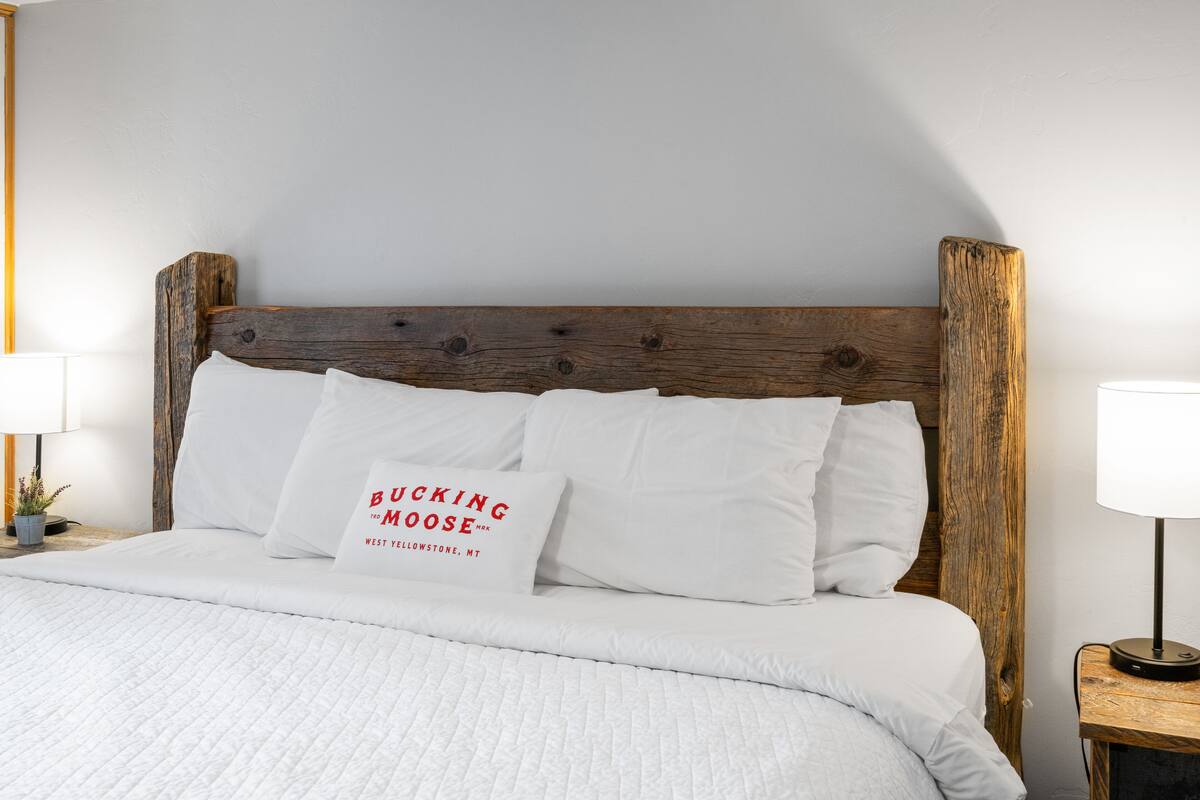 Una cama bien tendida con ropa blanca y un almohadón con texto.