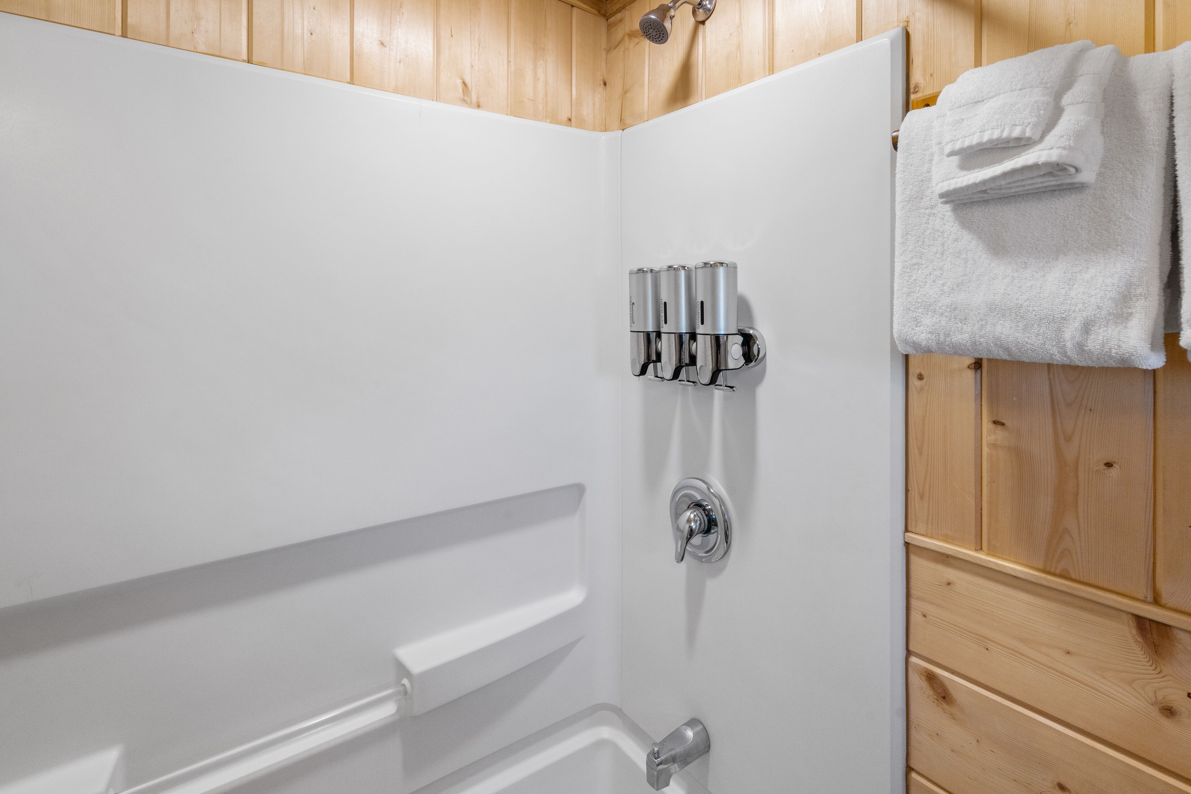 Un baño con techo de madera, paredes blancas, ducha con puerta de vidrio y toallero con toallas dobladas.