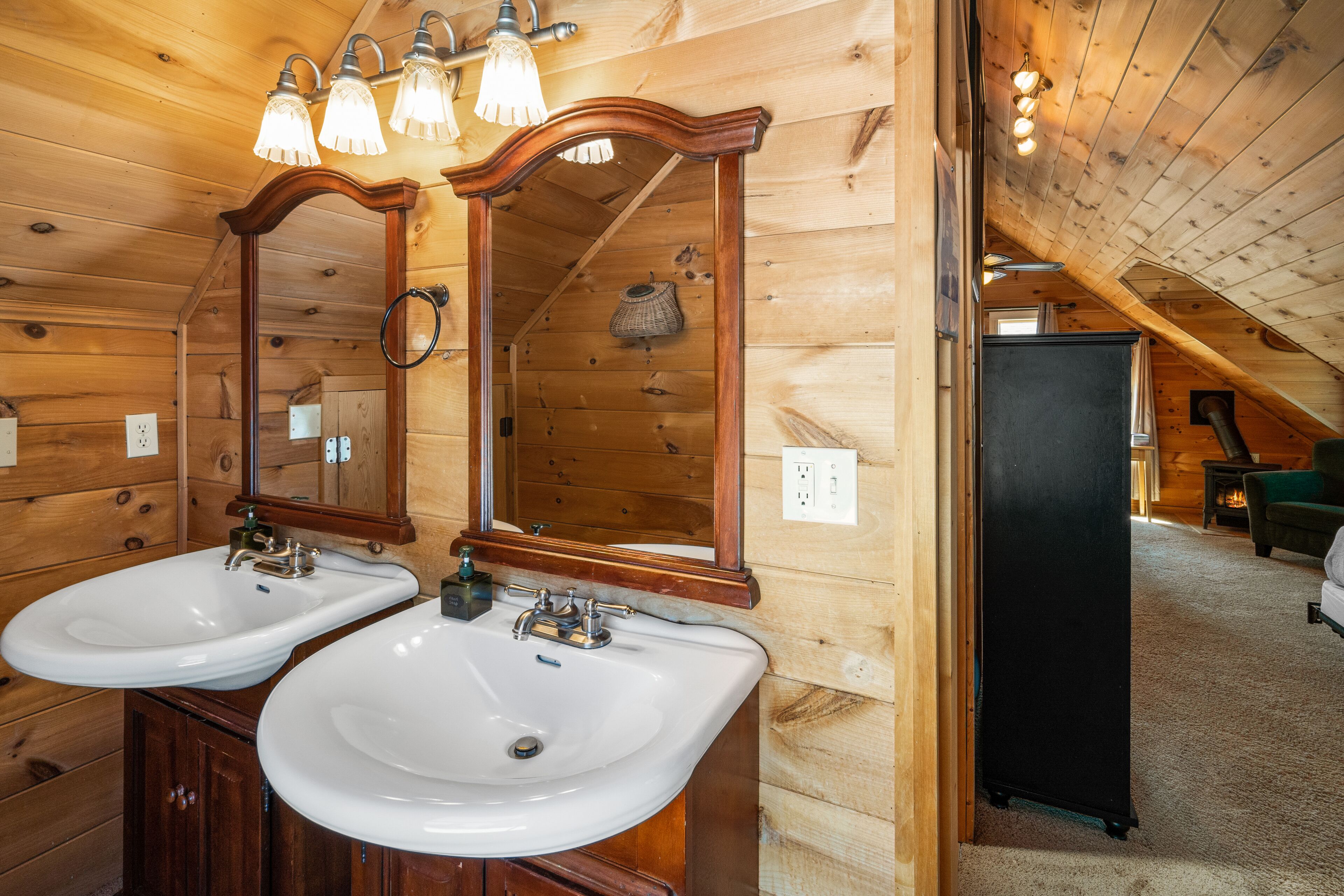 Baño de cabaña de madera con dos lavamanos, un espejo y una lámpara en el techo.