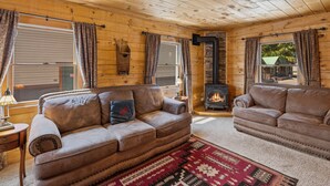 A cozy log cabin interior with two leather sofas, a fireplace, and wooden walls. - The Bucking Moose (West Yellowstone)