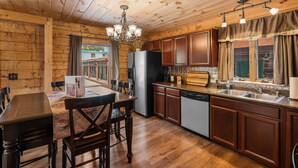A wooden-paneled kitchen with a dining table and chairs, a refrigerator, a dishwasher, and a window with curtains. - The Bucking Moose (West Yellowstone)
