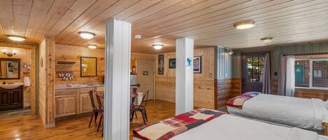 Una habitación tipo cabaña con pisos de madera, dos camas, kitchenette y baño.