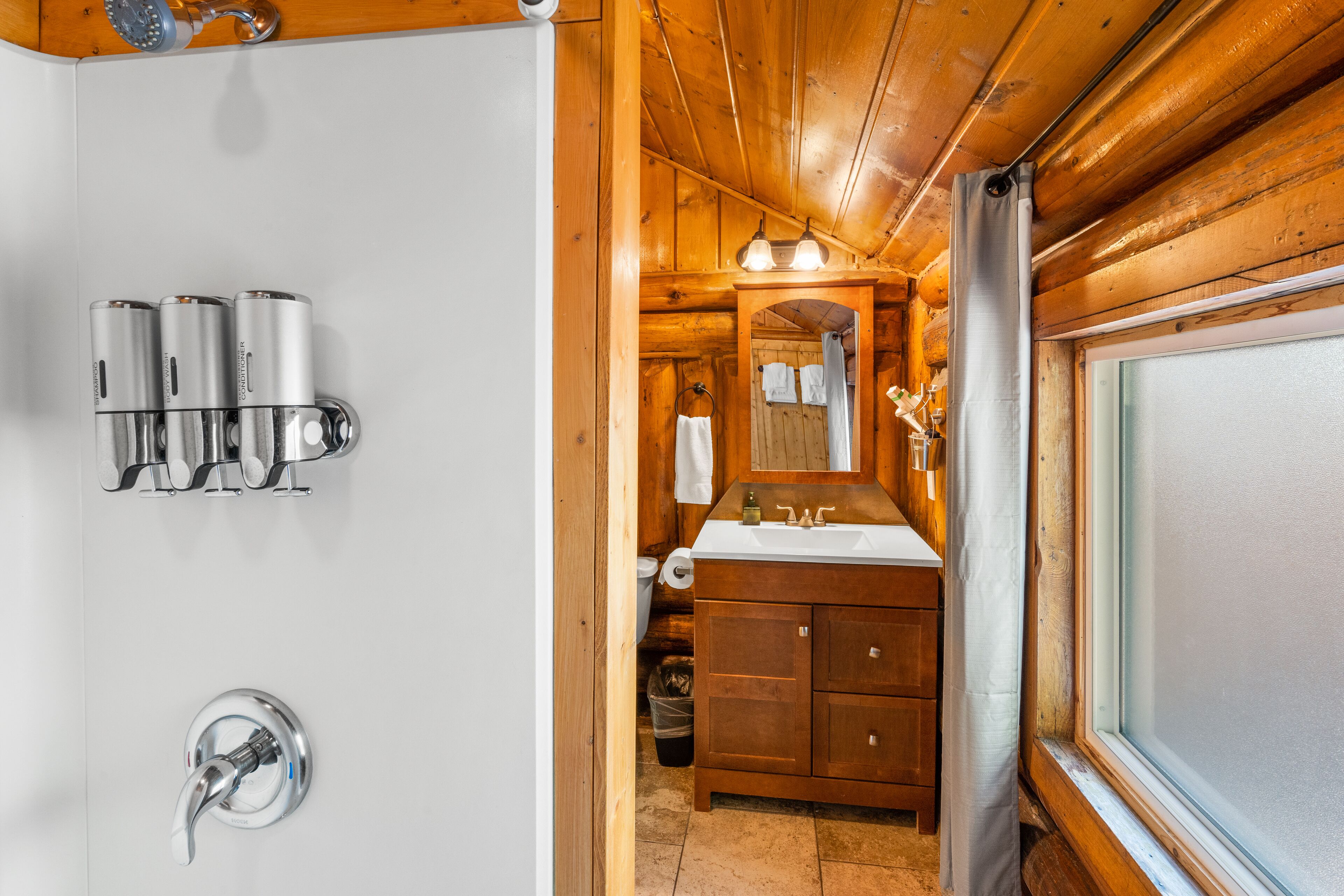 A wooden cabin bathroom with a sink, mirror, and three water dispensers.