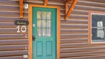 Une cabane en rondins avec une porte verte, une fenêtre donnant sur un beau paysage et une enseigne sur laquelle on peut lire « Cowboy 10 ».
